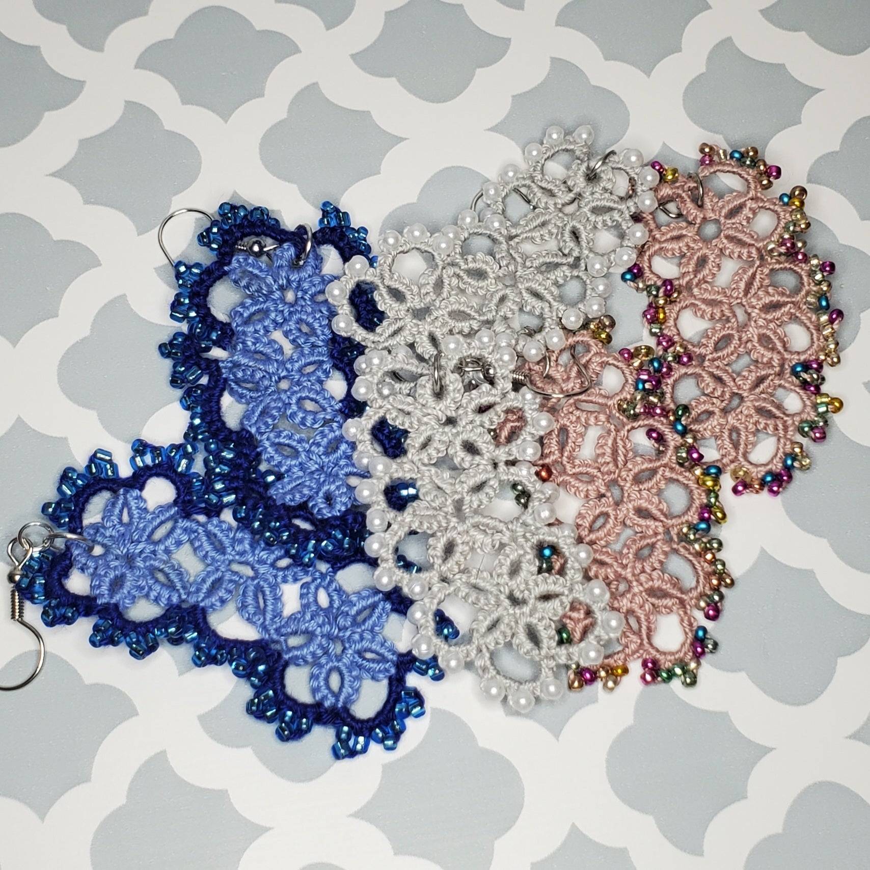 3 Jellybean Earrings Staged on grey and white patterned background, the earrings are 3 blues, grey pearl, and dusty mauve multi color