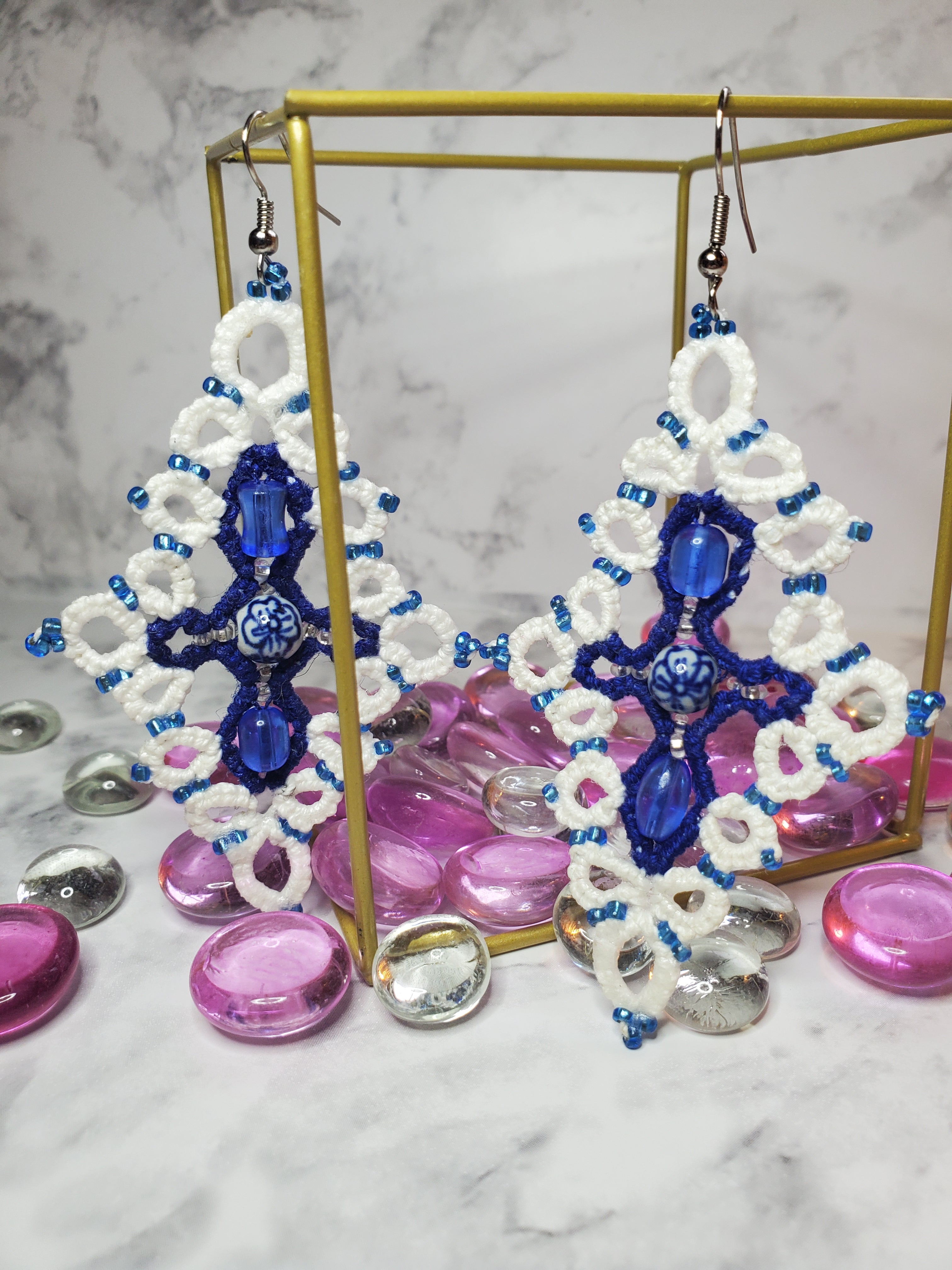 Custom White Blue Earrings Staged hanging from gold wire cube with pink and clear glass stones and a white marble background