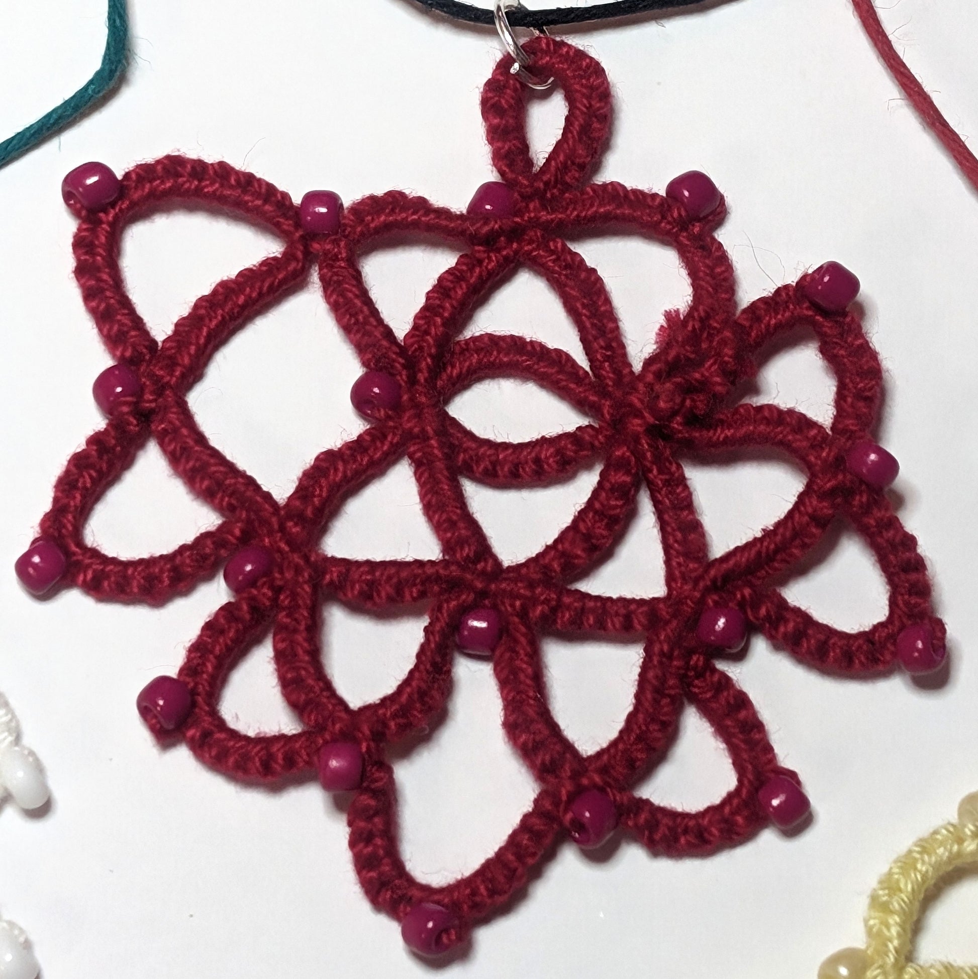 Reds Black Rose Necklace on white background with white yellow green red threads on outsdie