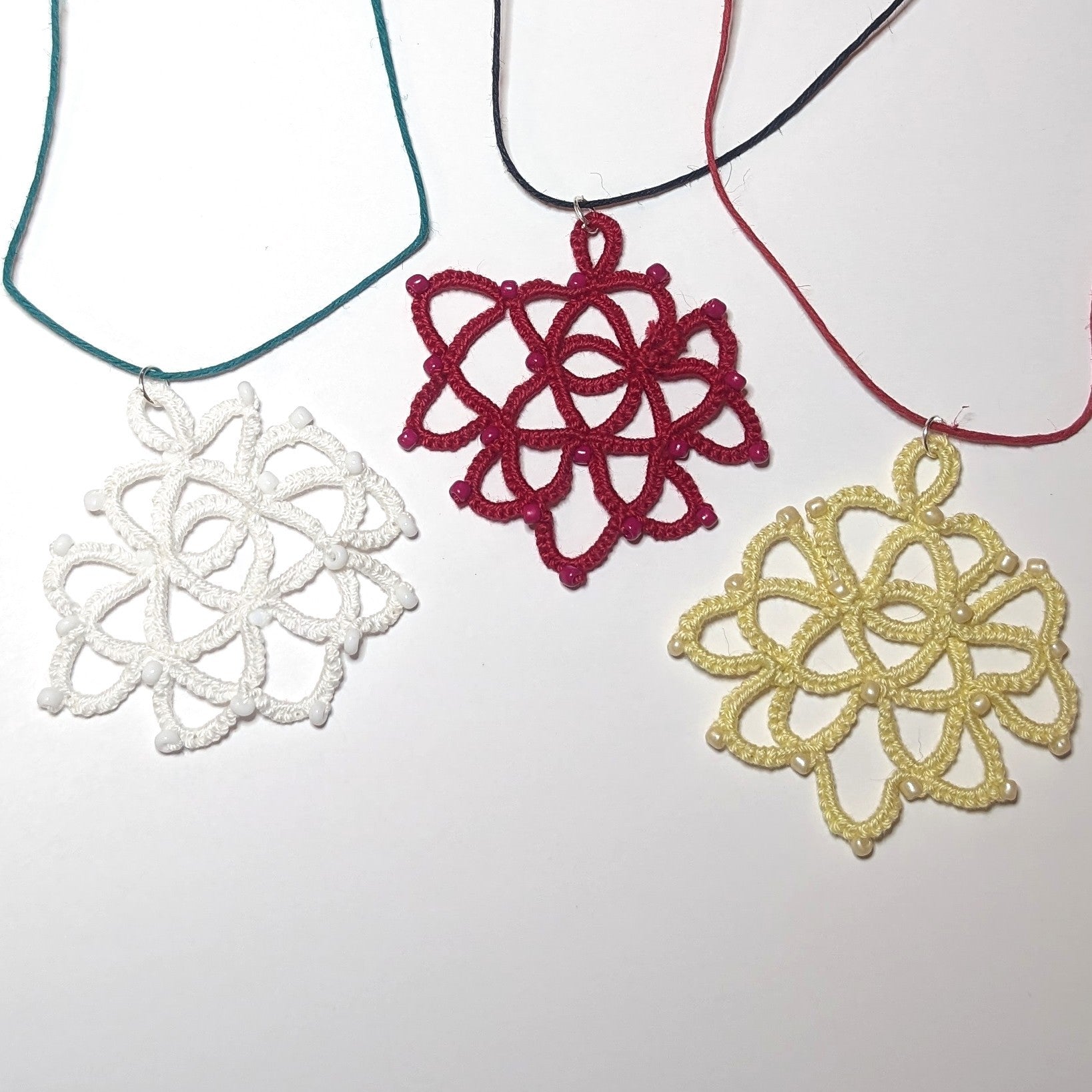 Trio Rose Necklace on white background, roses are white, red, and yellow, with green, black, and red corded necklace respectively